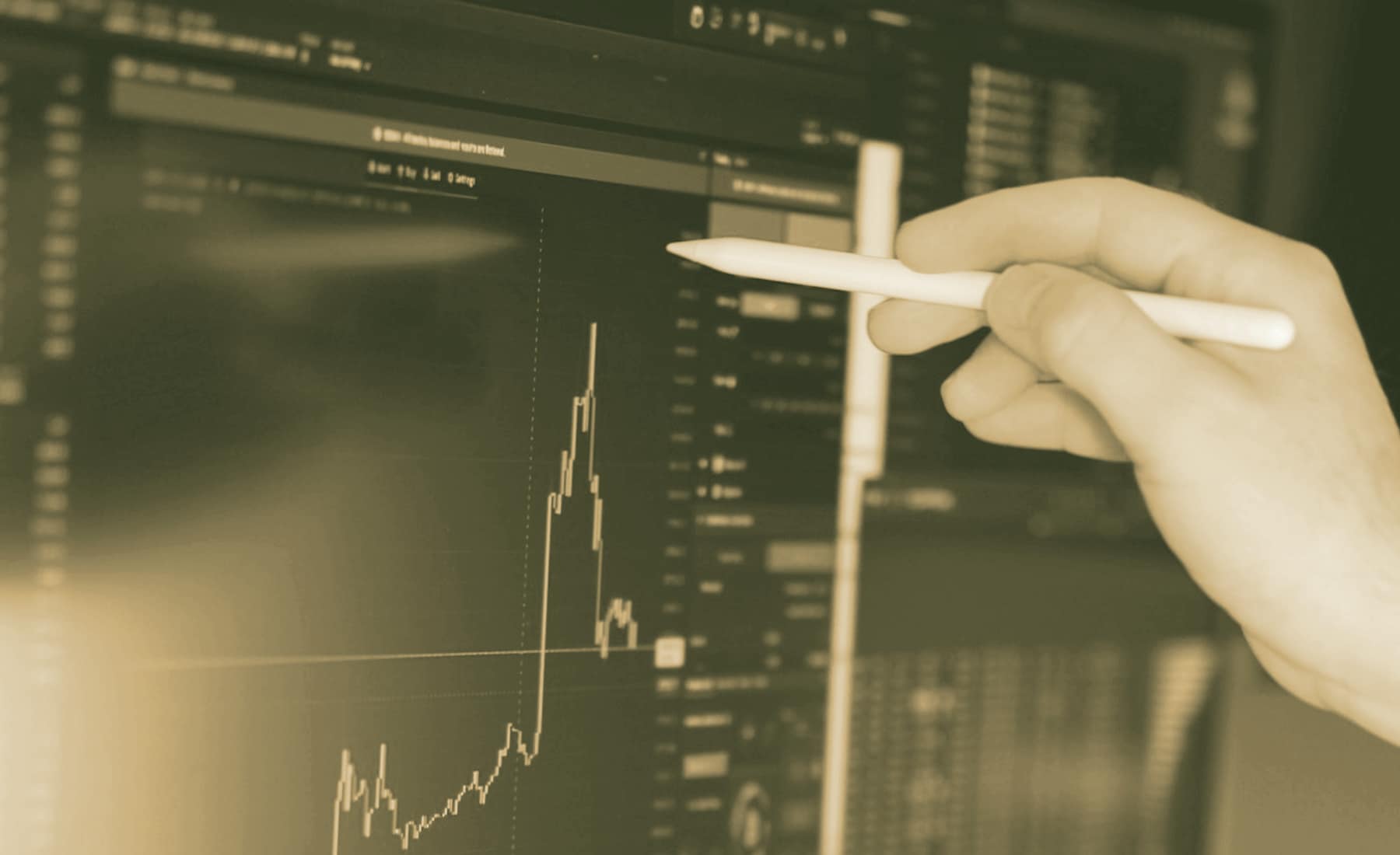 A hand marking a point on a candlestick chart on screen.