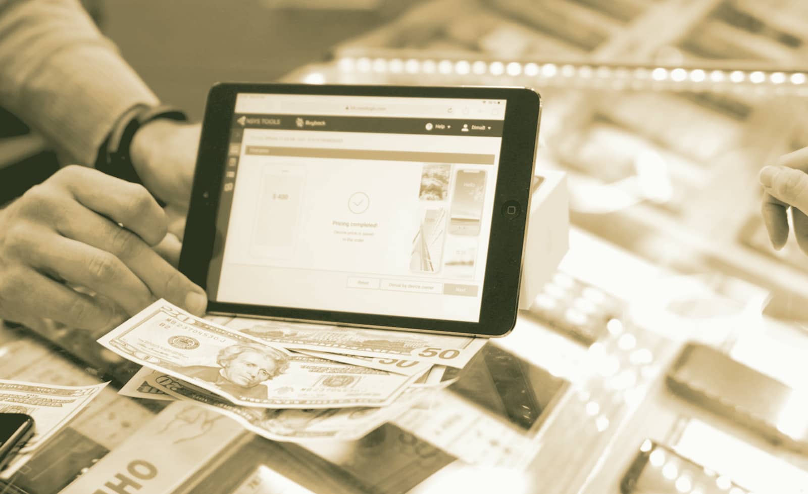 Hands at a tablet on a service counter, with banknotes beside it.